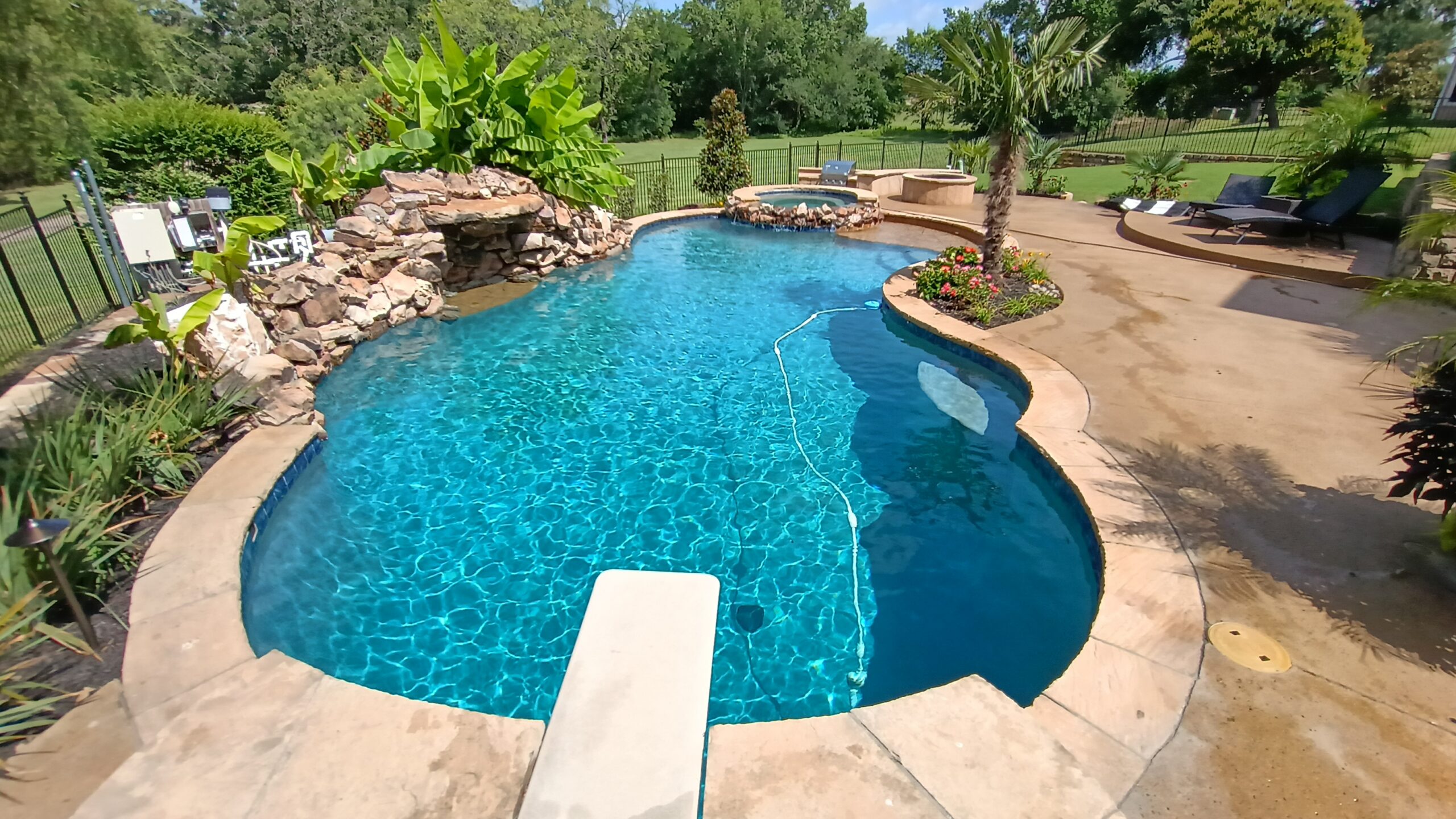 Luxury Backyard Pool with Diving Board, Rock Waterfall, and Spa in Texas Custom backyard pool with diving board, rock waterfall, raised spa, and tropical landscaping