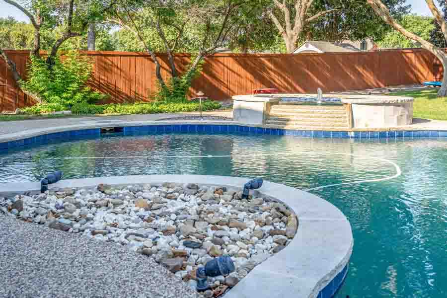 Weekly Pool Cleaning Service by Clear Choice Pool Care and Maintenance. Image of a jacuzzi in the background taken from a front angle in back of house. Image show decorative rock and lighting.
