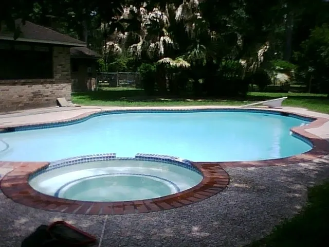 Weekly Pool Cleaning Service by Clear Choice Pool Care and Maintenance. Image of pool and jacuzzi in the foreground taken from a side angle in back of house.