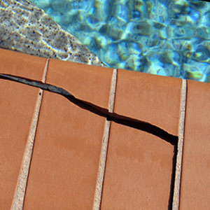 Photo showing a large crack at the edge of a pool. Tile is orange in color and water is blue.